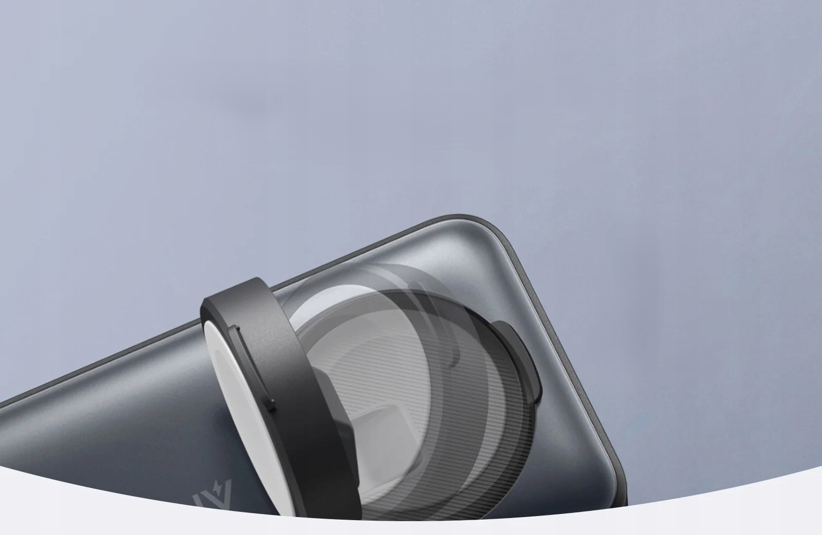 Zbliżenie telefonu z obiektywem i czarnym, okrągłym mocowaniem. Tło jest w kolorze jasnoszarym.