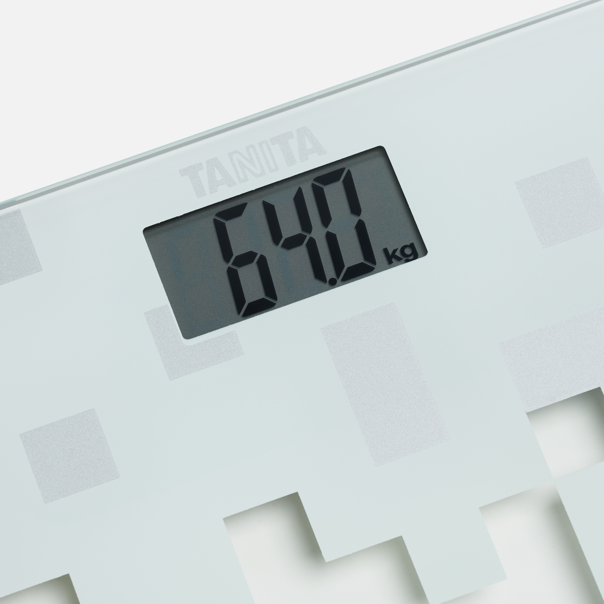 Een digitale weegschaal toont 64,0 kg. Het merk TANITA is zichtbaar. De weegschaal is wit met een patroon.