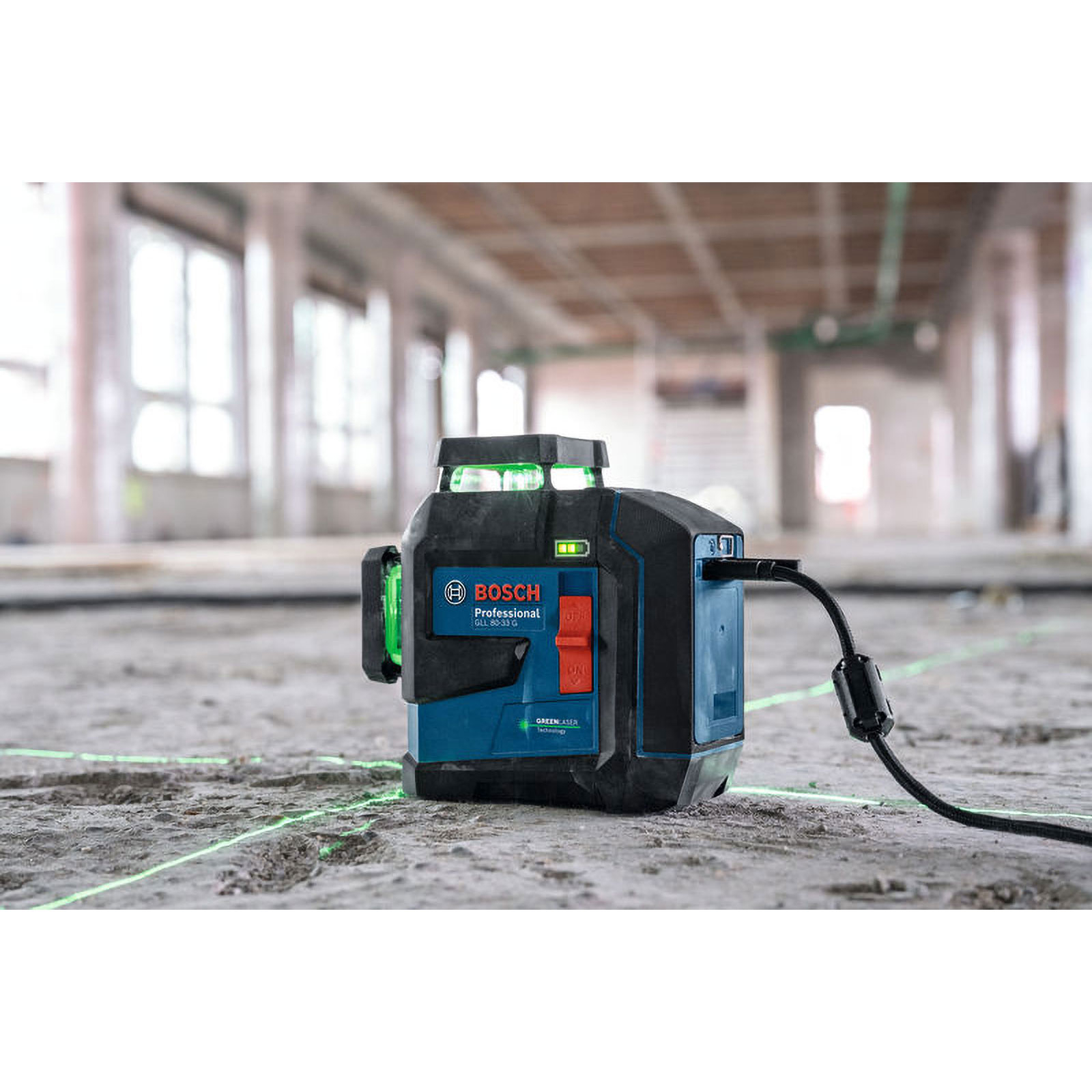 Ein professioneller Bosch-Laser projiziert grüne Linien auf Beton. Er ist blau und schwarz mit einem Stromkabel. Im Hintergrund ist eine Baustelle.