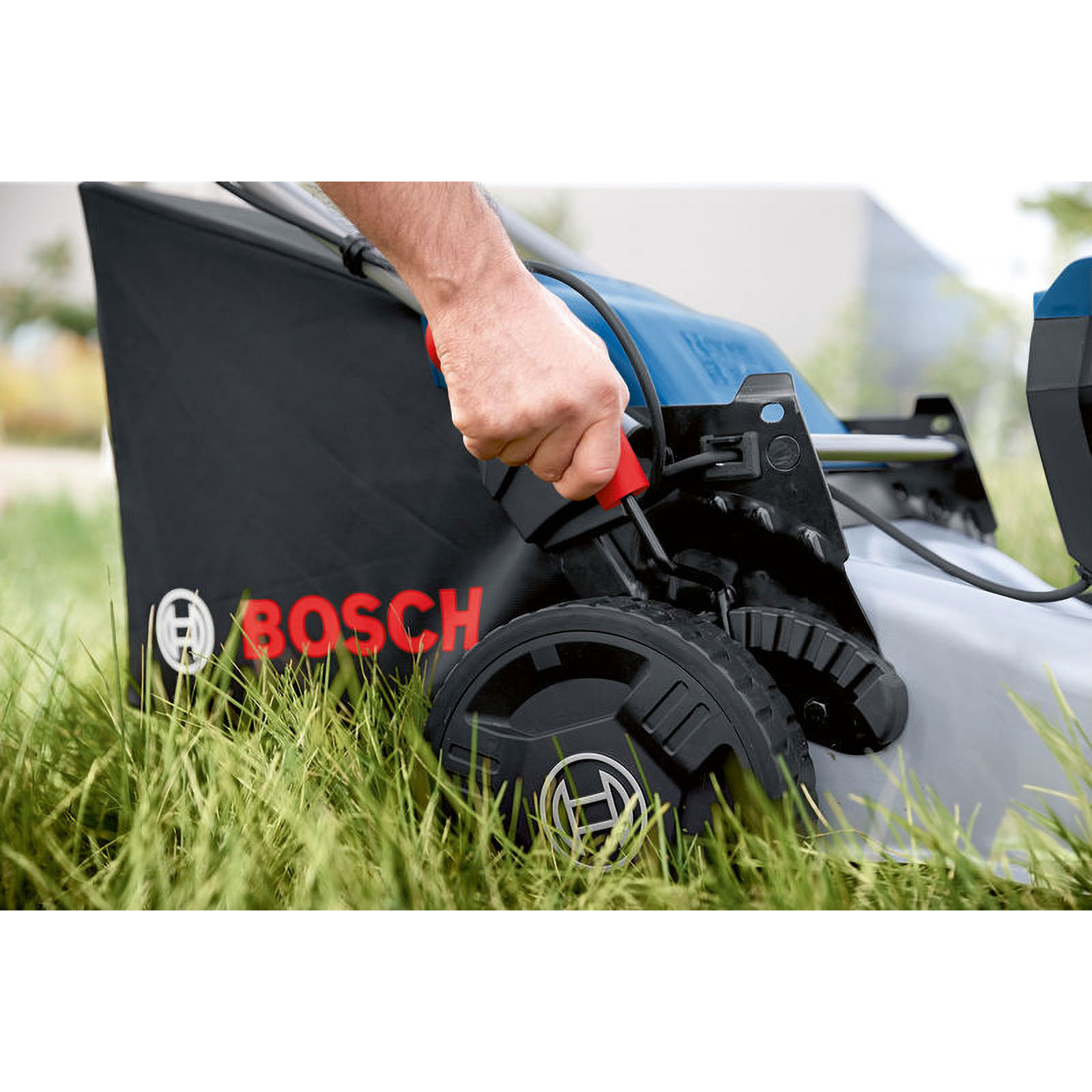 La mano de una persona sostiene el mango del cortacésped. El cortacésped es negro y azul, con el logotipo de Bosch, sobre un césped verde.