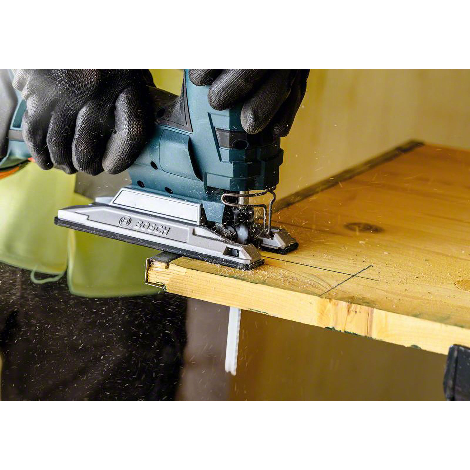 Una persona usa un seghetto alternativo Bosch per tagliare il legno. Mani con guanti neri tengono l'utensile su una tavola di legno.