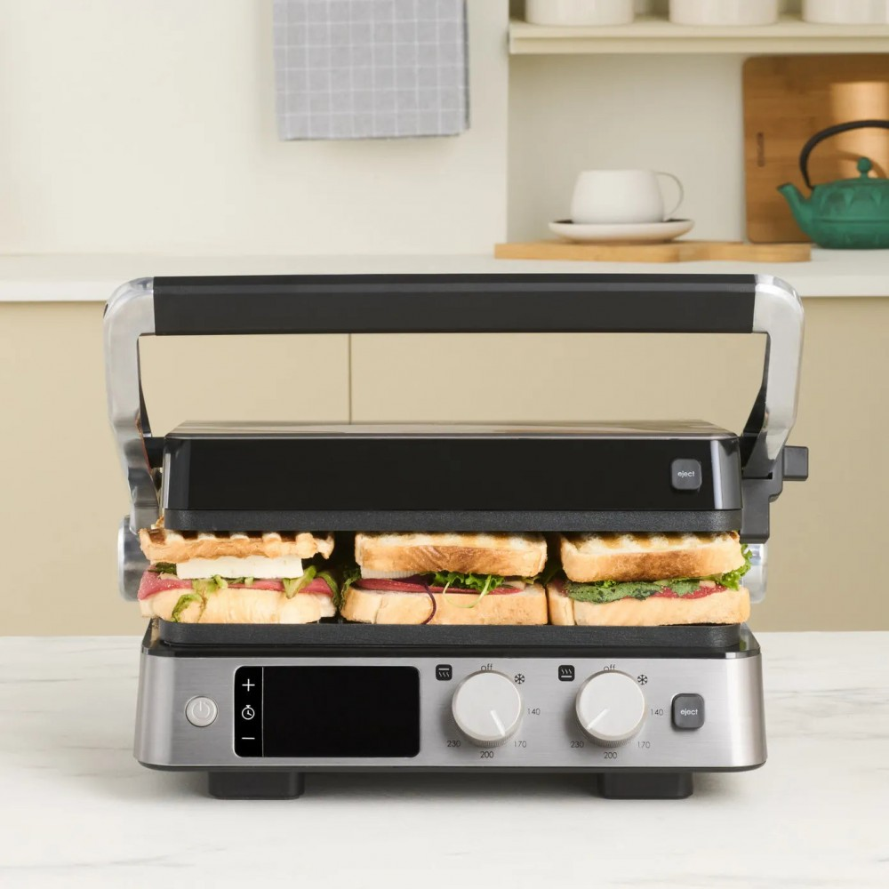 İçinde üç sandviç bulunan bir tost makinesi. Siyah bir üst kısma ve gümüş bir tabana sahip. Mutfak arkaplanı.