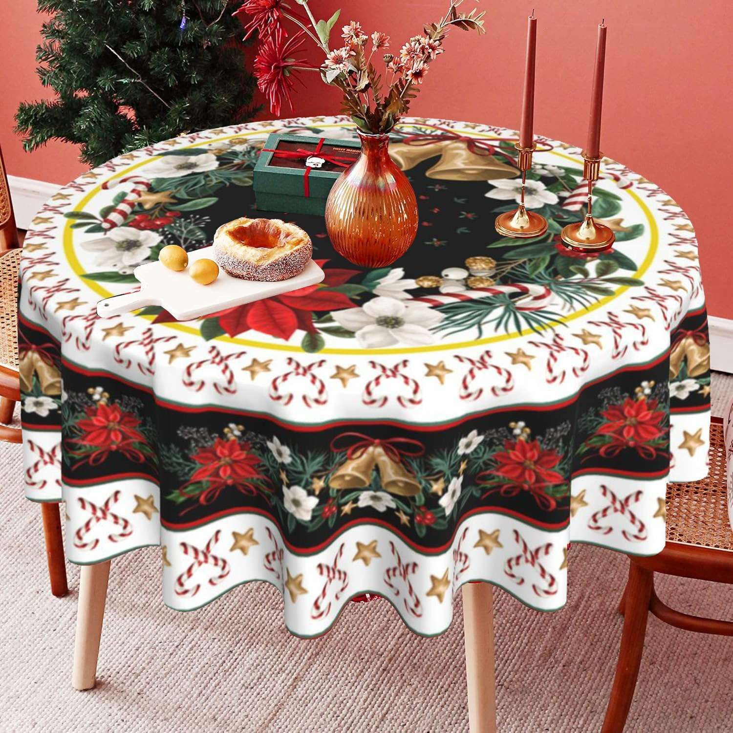 Ein runder Tisch mit einer weihnachtlichen Tischdecke. Geschenke, Essen, Kerzen und Blumen stehen auf dem Tisch, im Hintergrund ein Weihnachtsbaum.