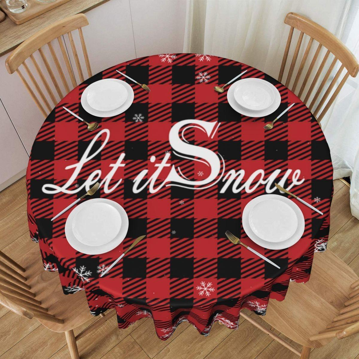 Ein runder Tisch mit einer rot-schwarz karierten Tischdecke mit der Aufschrift "Let it Snow". Es hat Teller, Gabeln, Löffel und Stühle.