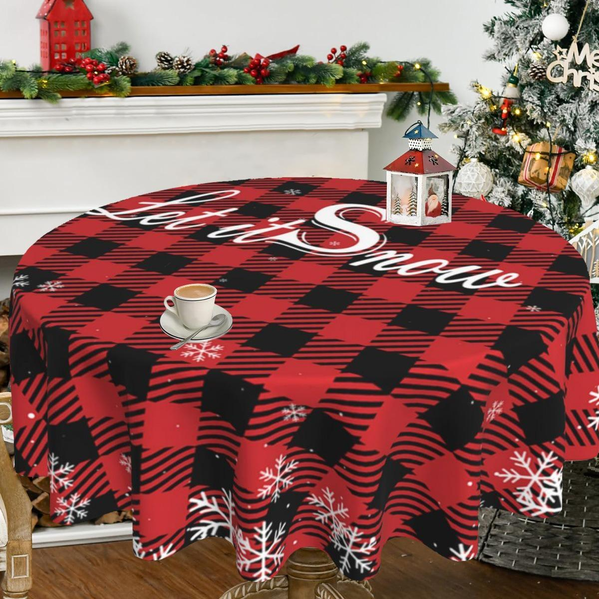 Ein runder rot-schwarz karierter Tischläufer mit der Aufschrift "Let it Snow". Eine Tasse Kaffee steht auf dem Tisch. Im Hintergrund ein Weihnachtsbaum.