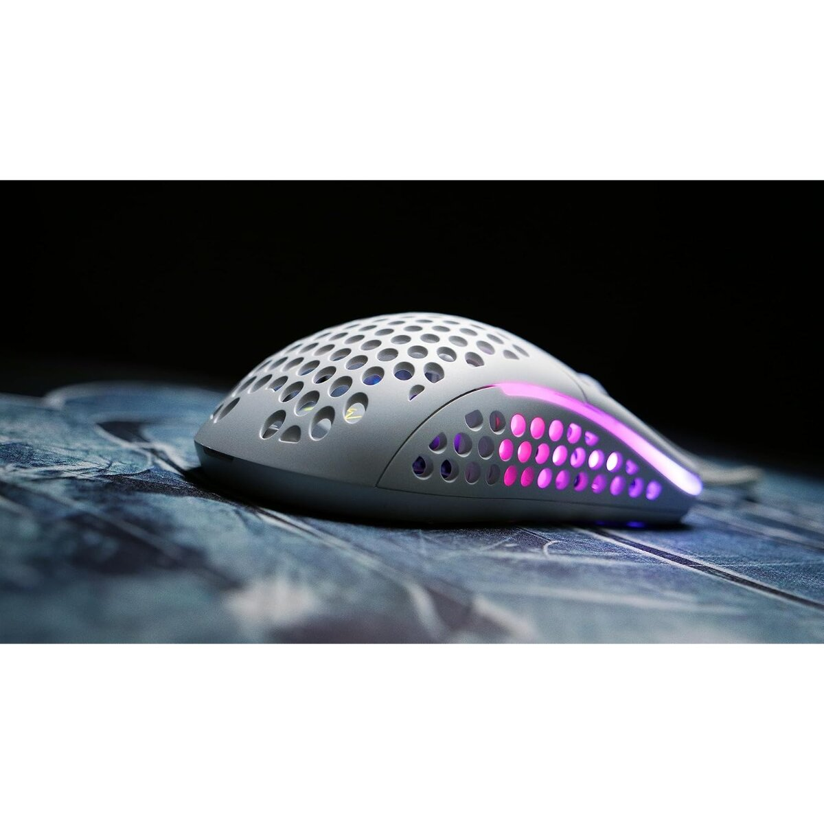Un mouse da gaming bianco con design perforato e illuminazione RGB, poggia su una superficie a motivi blu e grigi, su sfondo scuro.