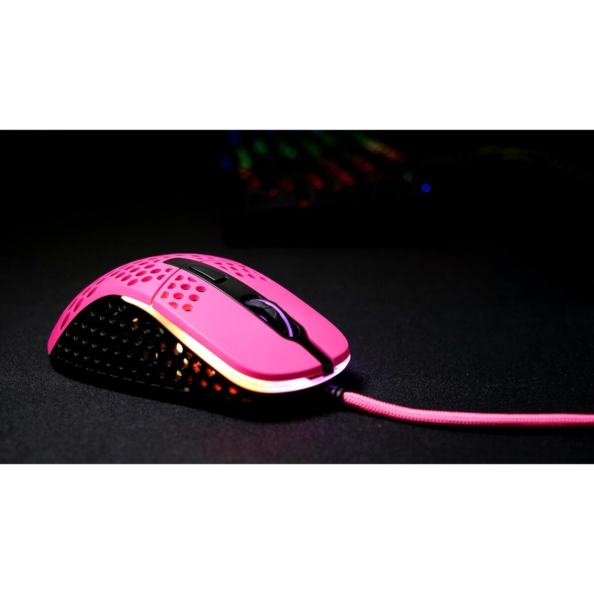 A pink gaming mouse with a black top and bottom. The mouse is on a black surface, and has a pink cable.