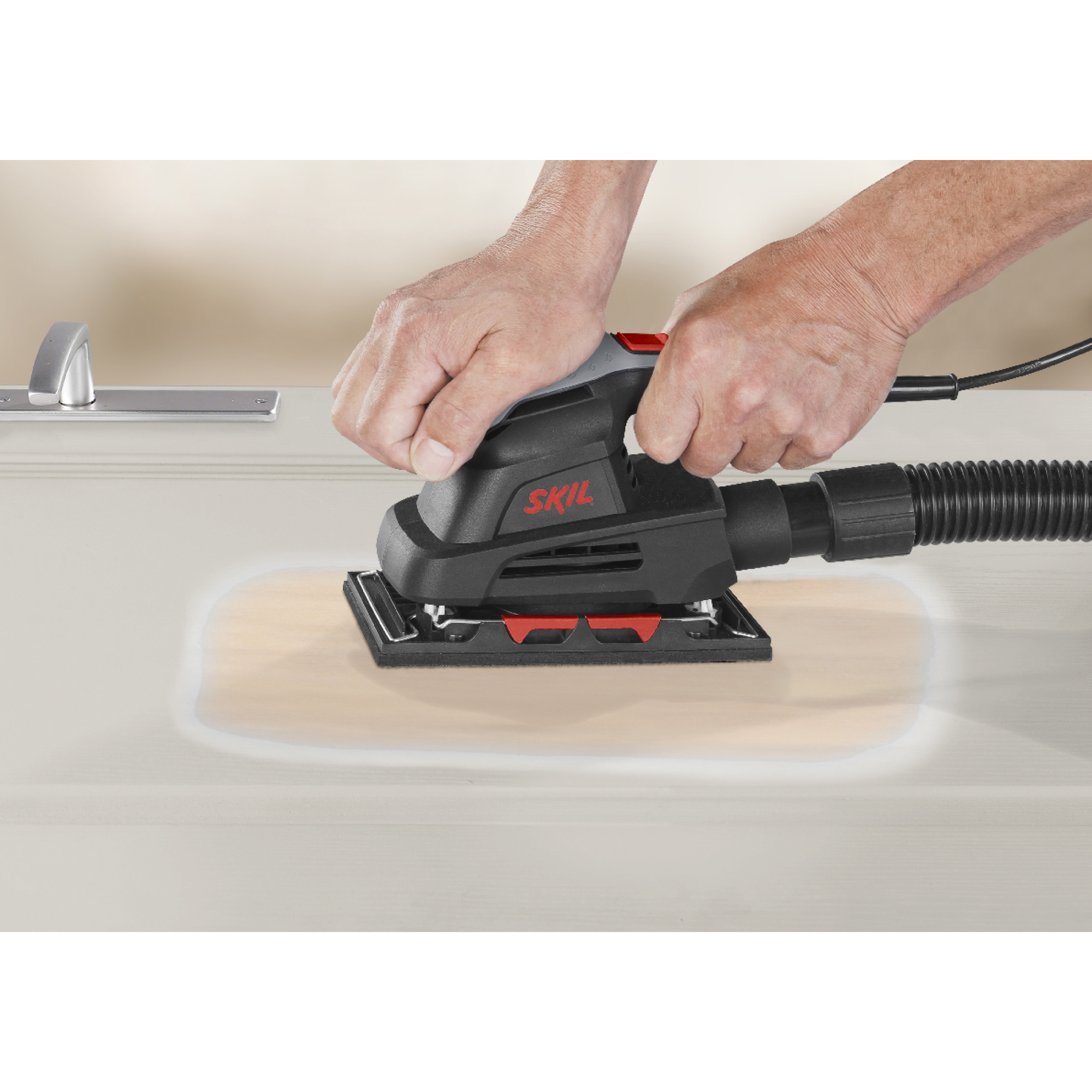 A person using a black SKIL sander on a light-colored wooden surface. The hands are holding the sander.