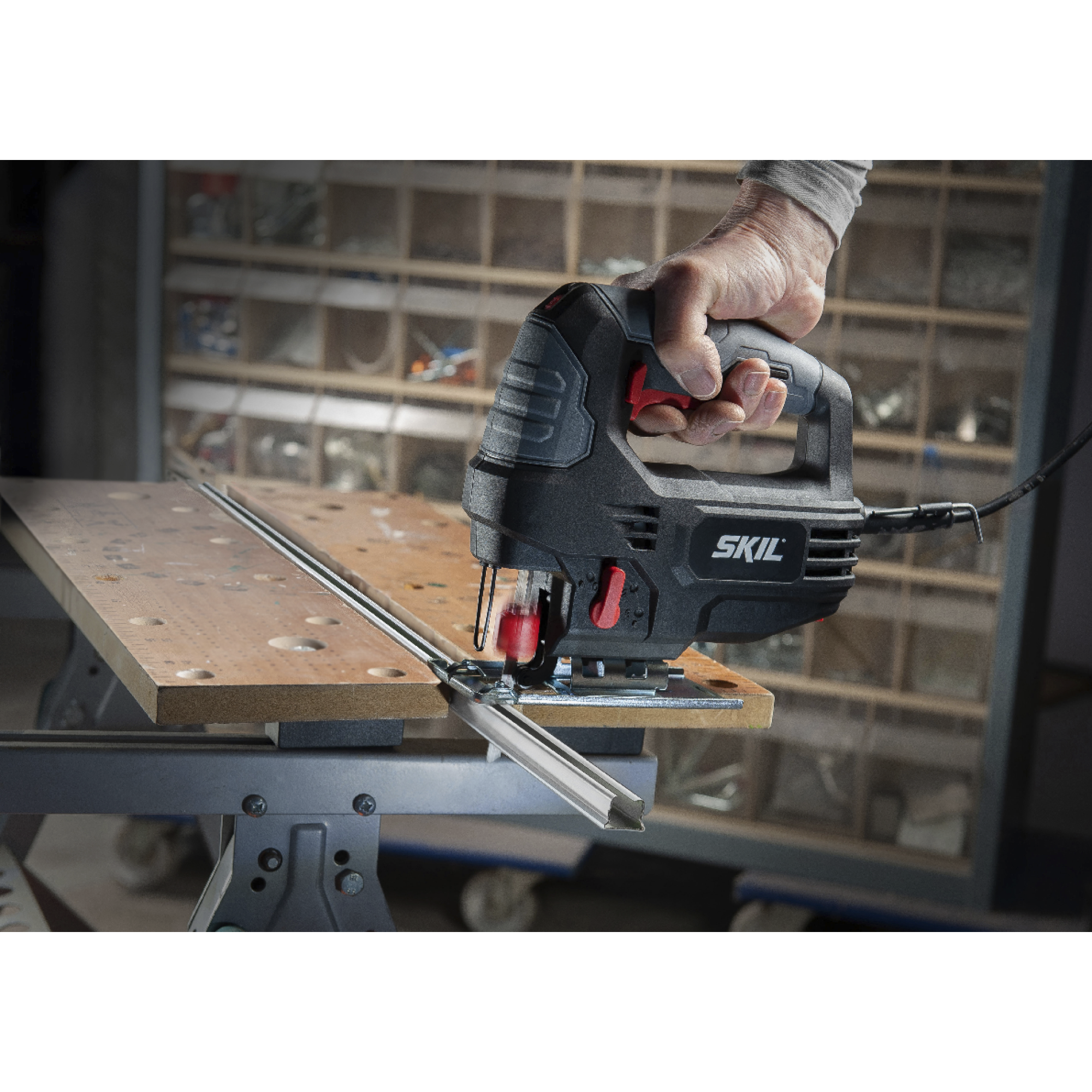Een hand houdt een zwarte decoupeerzaag vast die hout snijdt. Het gereedschap staat op een werkbank, en er is opslag op de achtergrond.