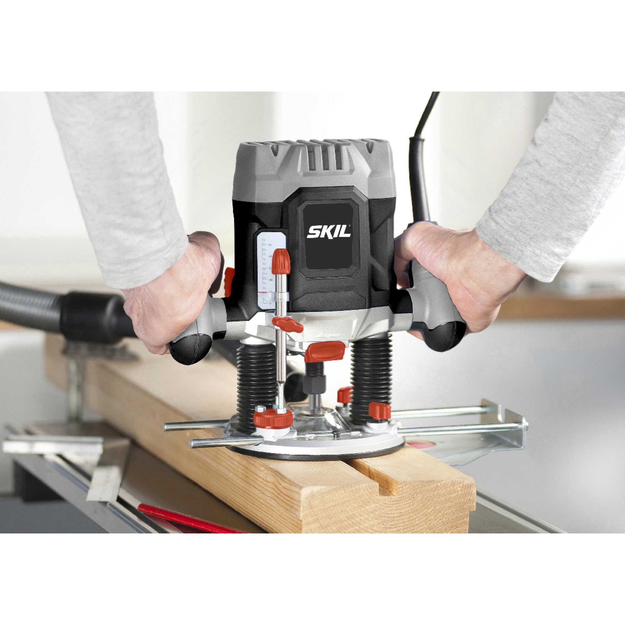Een persoon die een SKIL-freesmachine gebruikt om een houten plank te zagen. De machine is zwart en grijs, en de handen zijn zichtbaar.
