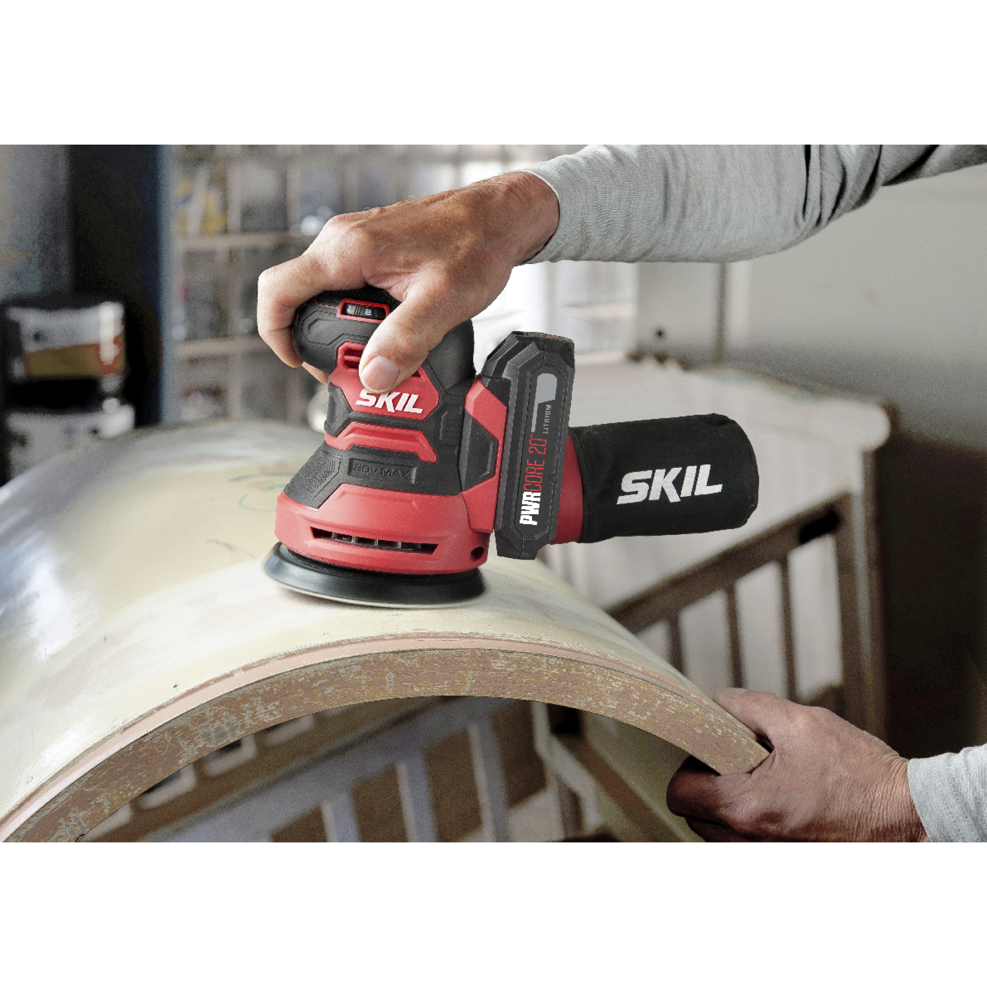 Een persoon schuurt een houten oppervlak met een rood-zwarte schuurmachine, handen zichtbaar. De schuurmachine heeft 'SKIL' erop.