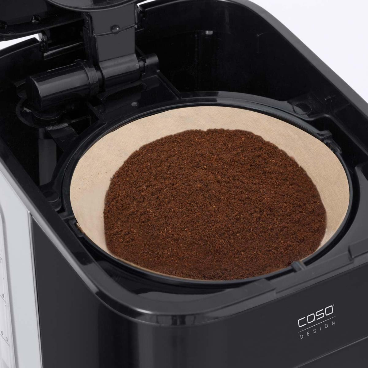 Innenraum der Kaffeemaschine mit einem Filter, der mit Kaffeepulver gefüllt ist. Die Maschine ist schwarz, der Filter ist beige.