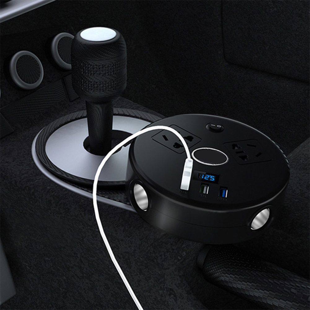 Schwarzer Auto-Netzadapter mit Steckdosen, USB-Anschlüssen und Digitalanzeige. Ein weißes Kabel ist eingesteckt. Der Schalthebel ist im Hintergrund.