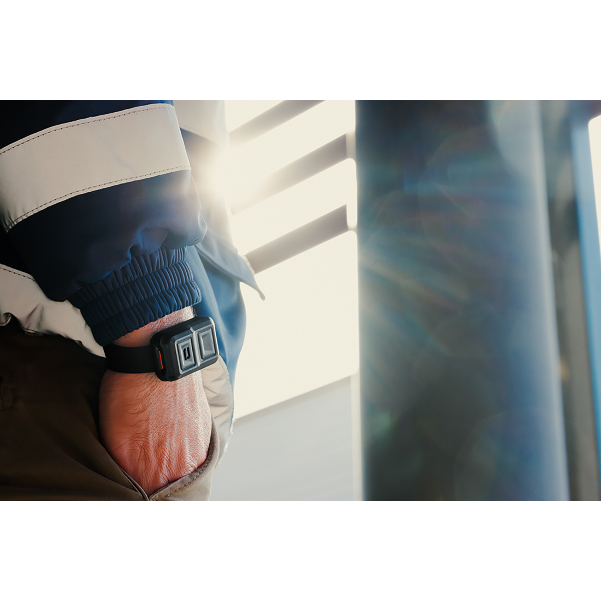 Eine Person mit einem schwarzen Armband mit zwei Quadraten hält ihre Hand in der Tasche. Die Person trägt eine Jacke.