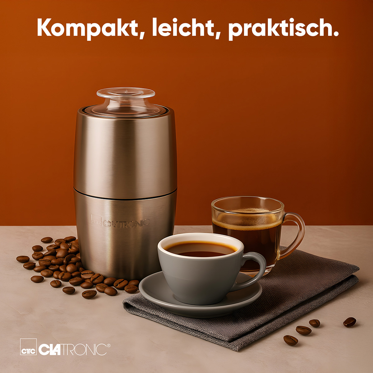 Eine Kaffeemühle, zwei Tassen Kaffee und Kaffeebohnen sind auf einem Tisch angeordnet. Der Hintergrund ist ein brauner Farbverlauf.