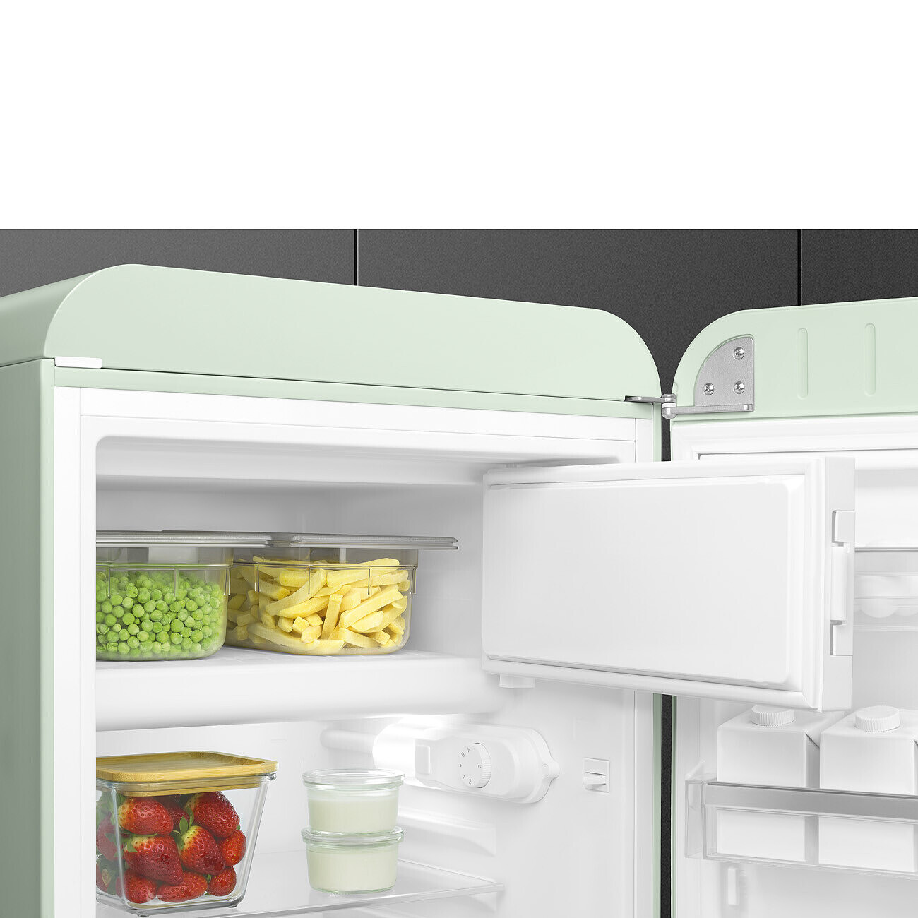 Un refrigerador con la puerta abierta, mostrando recipientes de guisantes, papas fritas, fresas y yogur. El refrigerador tiene un exterior verde claro.