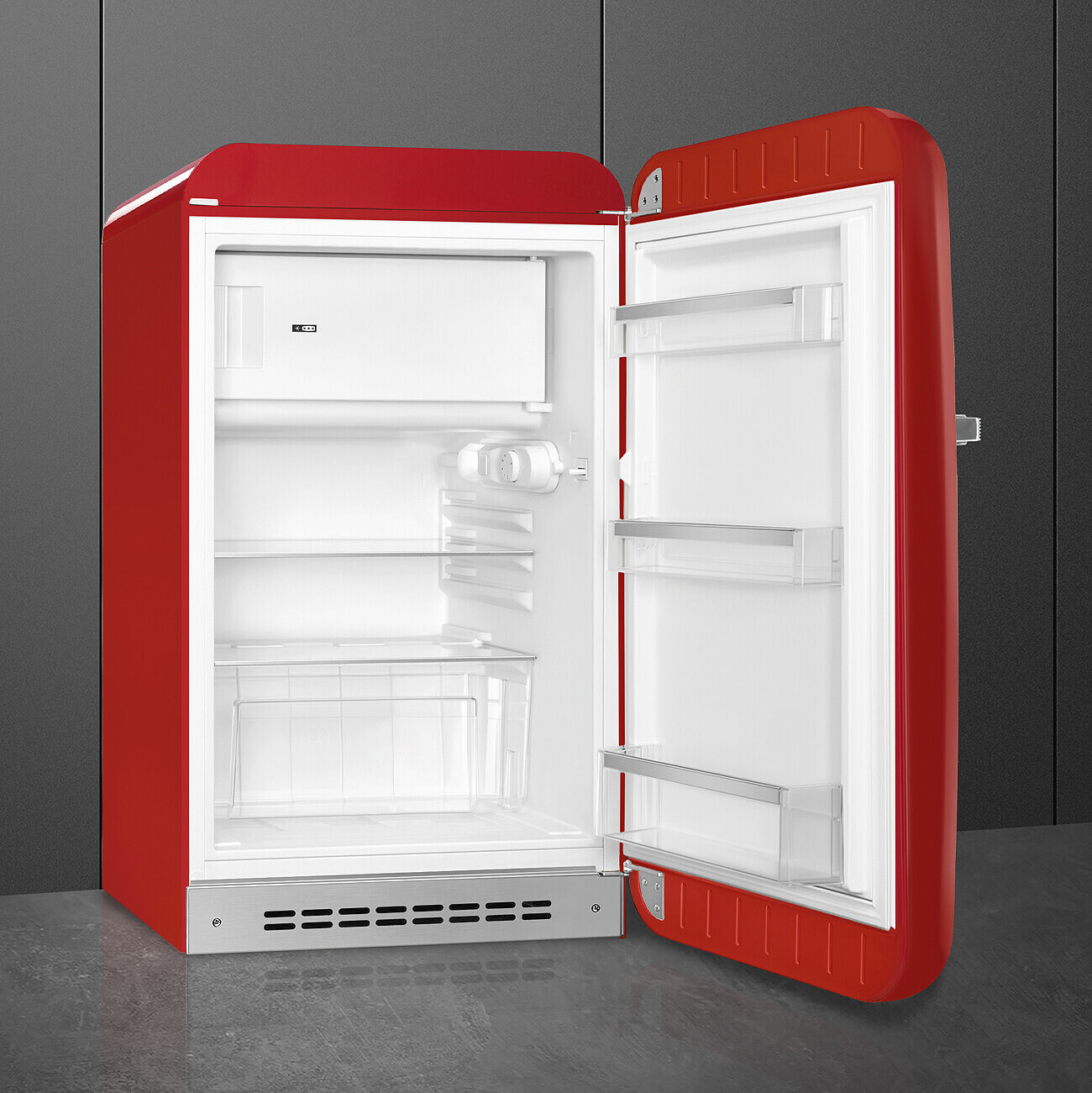 Ein roter Retro-Kühlschrank mit offener Tür. Innen befinden sich Regale und ein Gefrierfach. Der Hintergrund ist eine graue Wand.