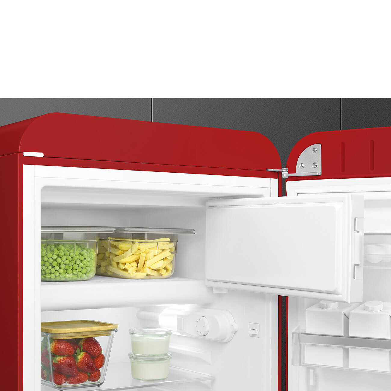 Ein roter Retro-Kühlschrank ist geöffnet. Innen sind Erbsen, Pommes, Erdbeeren und Milchprodukte zu sehen. Die Tür ist offen.