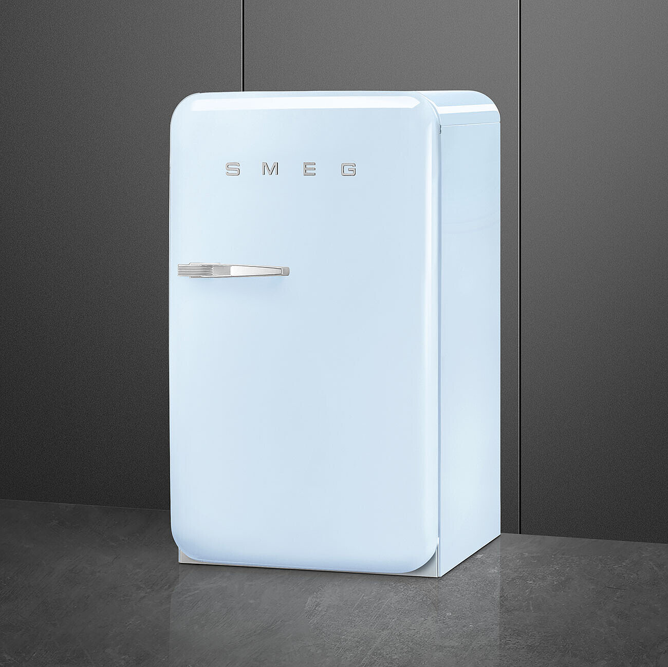 Un refrigerador Smeg celeste sobre una superficie gris oscuro. El fondo es una pared gris oscuro.
