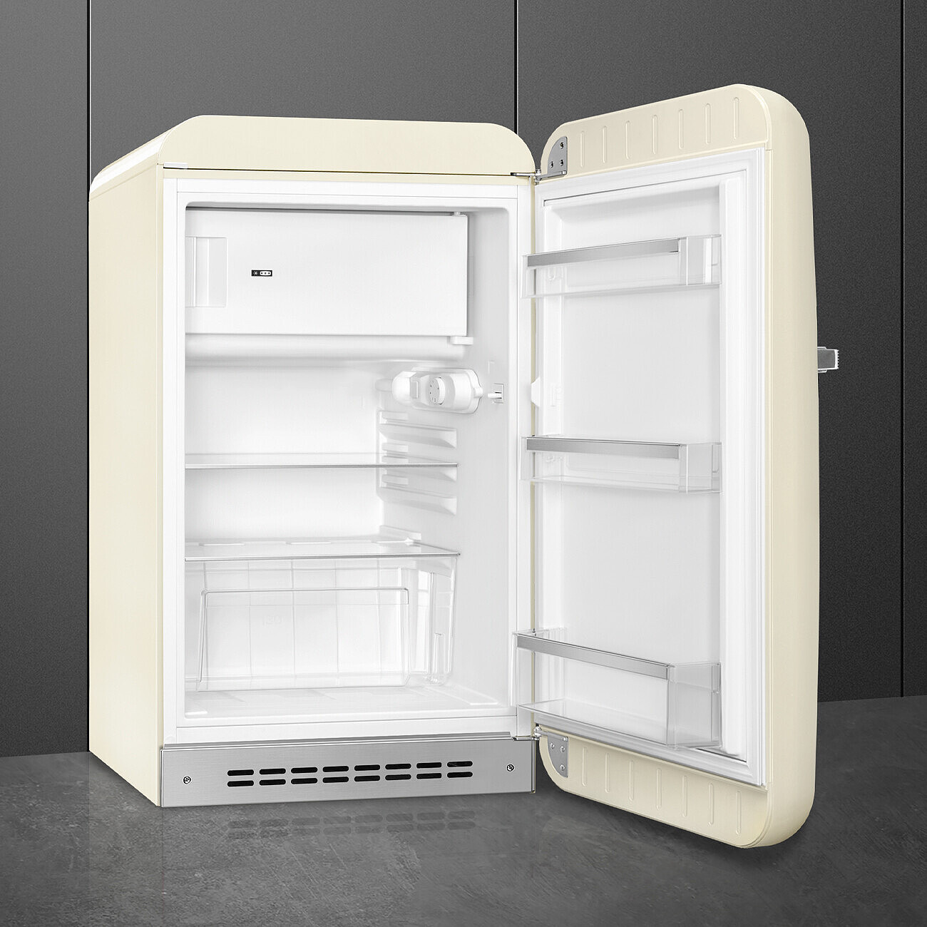 Un refrigerador crema abierto. Dentro, estantes y un pequeño congelador. La puerta está abierta, revelando detalles interiores. Colocado sobre una superficie gris.