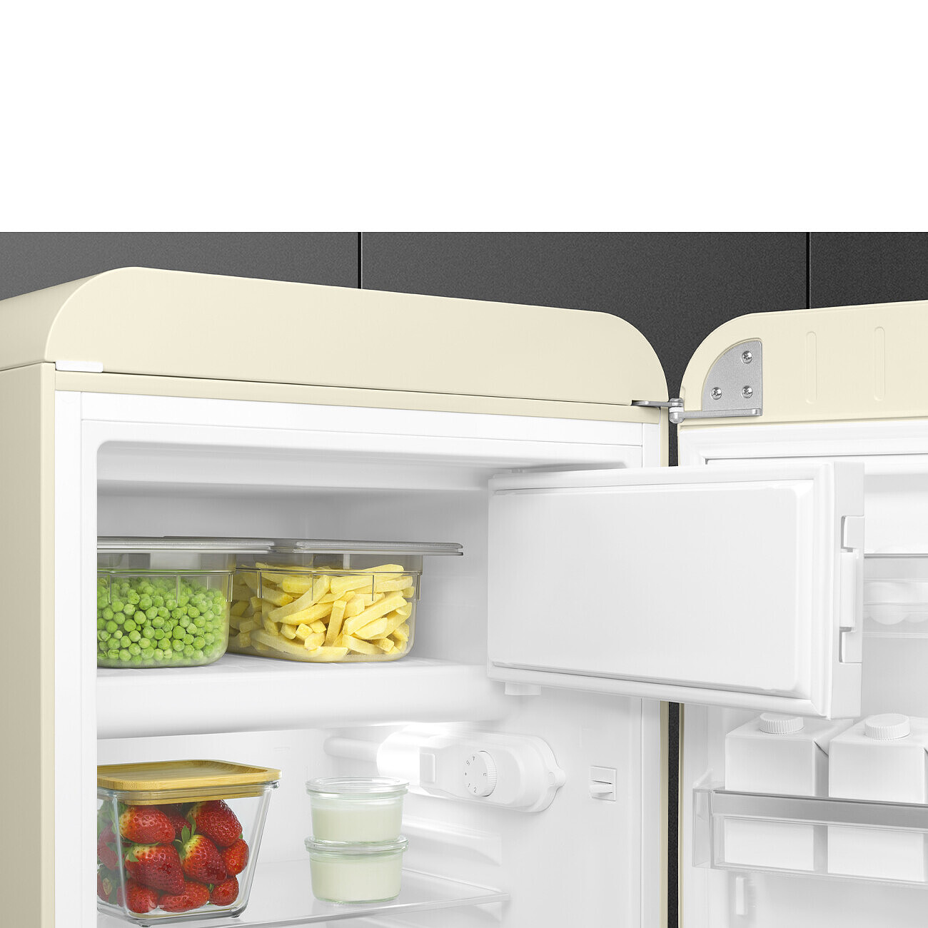 Un refrigerador beige abierto. Dentro hay recipientes con guisantes, papas fritas, fresas y yogur. Un cajón del congelador está abierto. El fondo es gris.