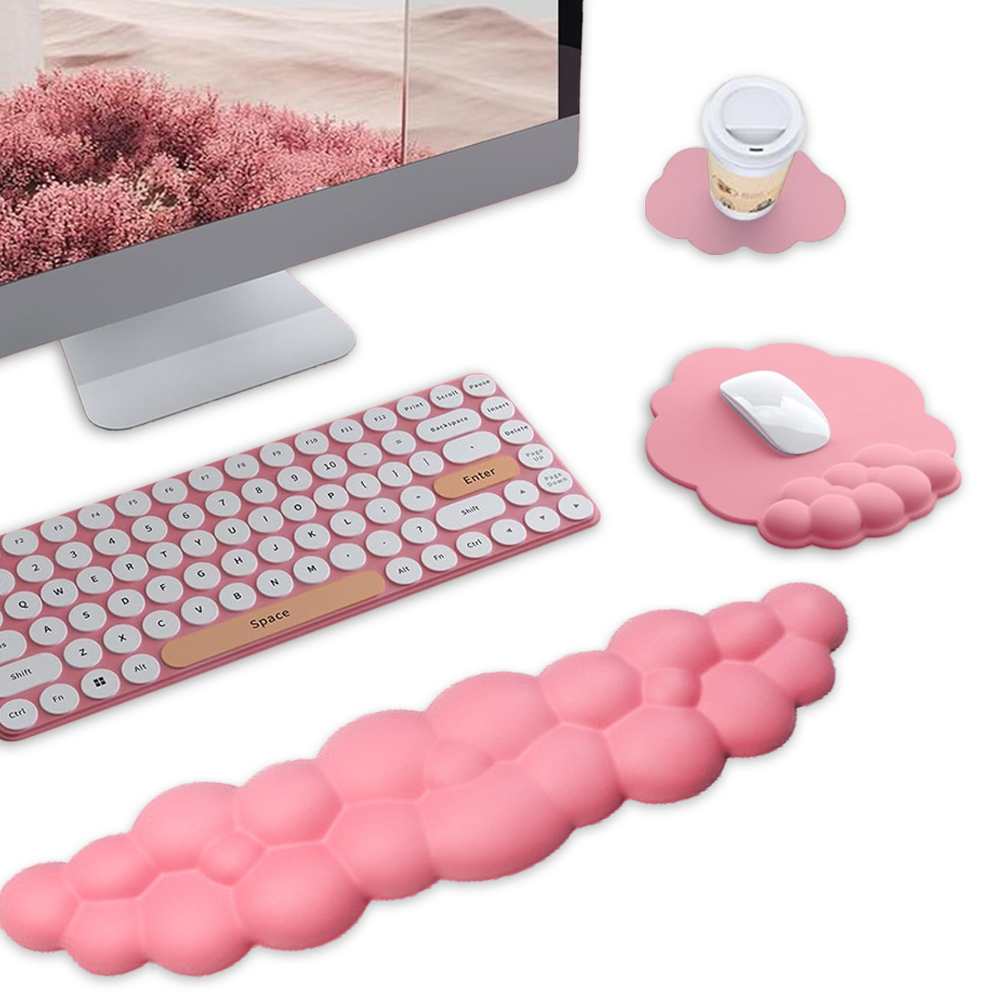 Eine rosa Tastatur, ein Mauspads und eine Handgelenkstütze liegen neben einem Computer. Ein Becher steht auf einem wolkenförmigen Untersetzer.