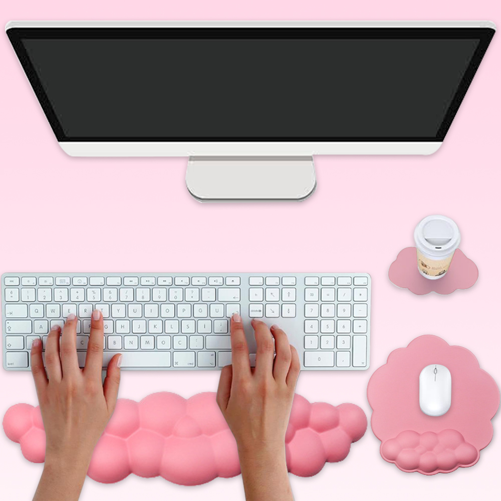 Computereinrichtung auf rosa Hintergrund. Hände tippen auf einer Tastatur. Ein Monitor, ein Mauspads und eine Kaffeetasse sind sichtbar.