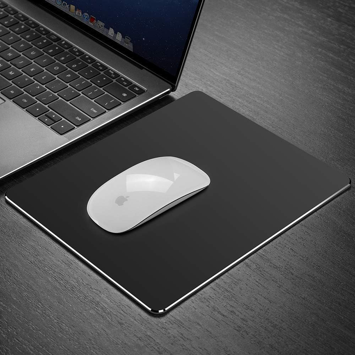 Ein Laptop mit schwarzer Tastatur und eine weiße Maus auf einem schwarzen Mauspads, platziert auf einem Holztisch. Der Hintergrund ist unscharf.