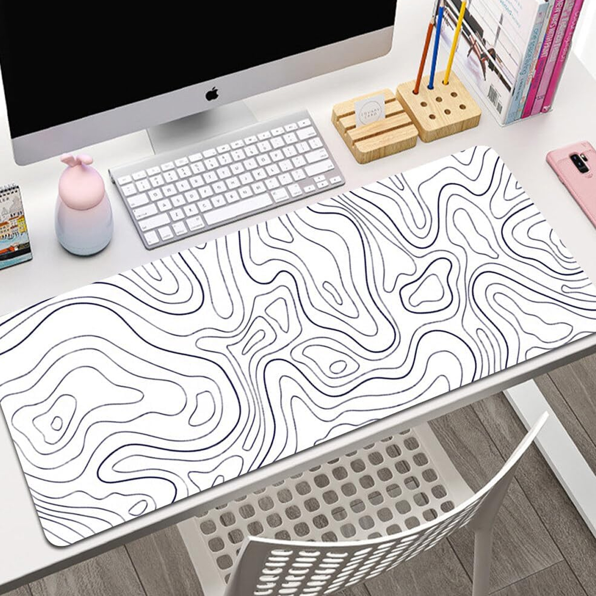 Ein weißer Schreibtisch mit Computer, Tastatur und einer Mausunterlage mit topografischem Kartendesign. Ein rosa Telefon und andere Büromaterialien sind sichtbar.
