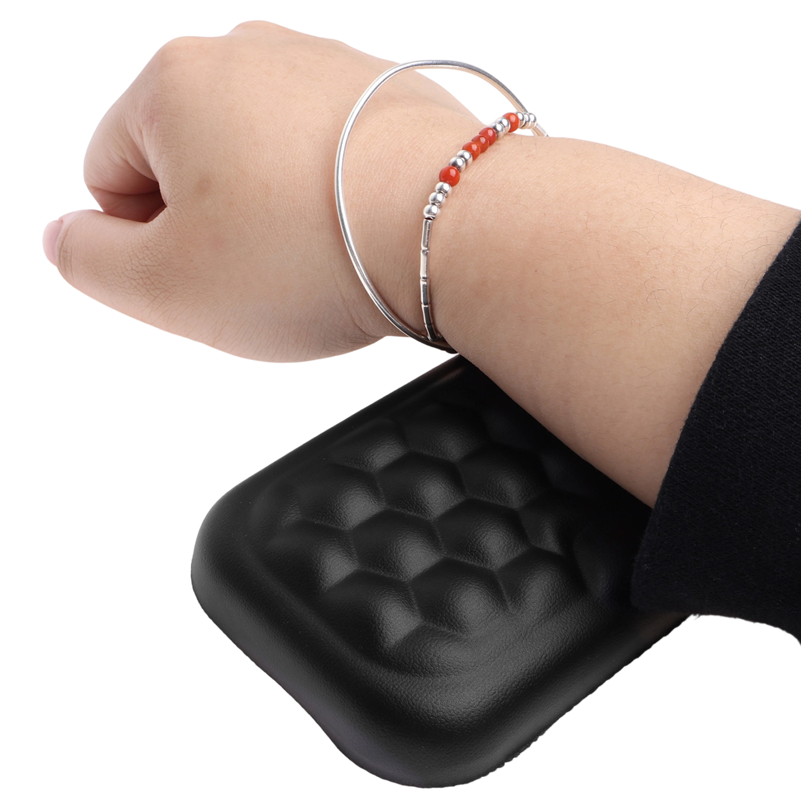 Ein Arm mit Armband und ein schwarzes Objekt mit strukturierter Oberfläche. Das Armband hat rote Perlen.
