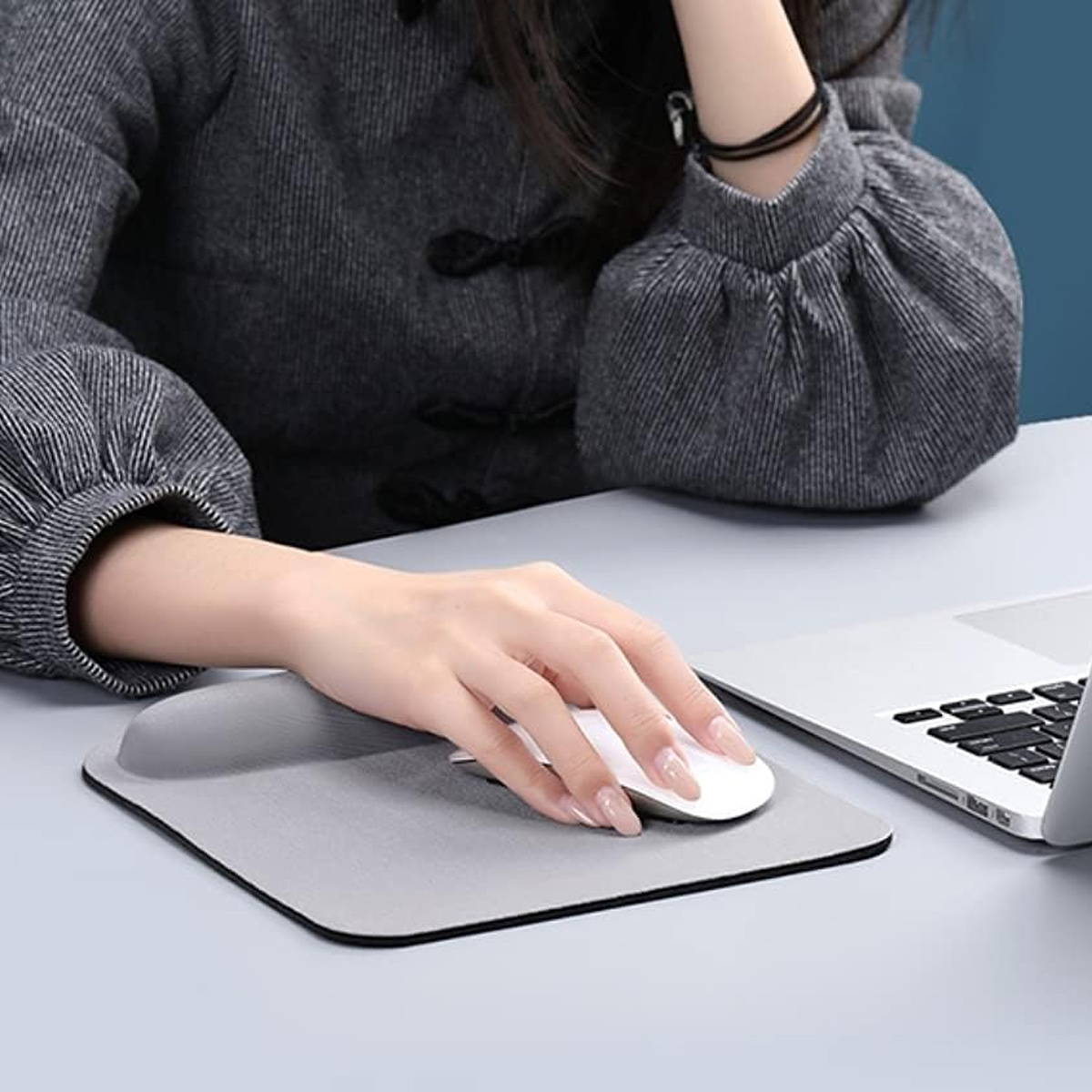 Eine Person benutzt eine Maus auf einem Mauspads neben einem Laptop. Die Person trägt ein graues Hemd. Die Szene ist an einem Schreibtisch.