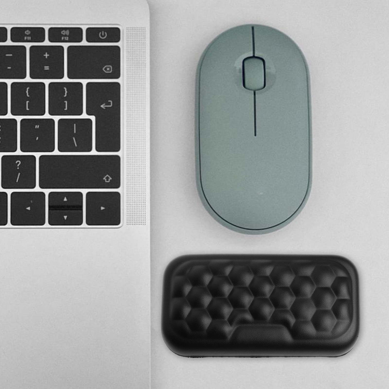 Eine Laptop-Tastatur, eine graue Maus und eine schwarze Handgelenkstütze. Die Gegenstände befinden sich auf einer weißen Oberfläche.