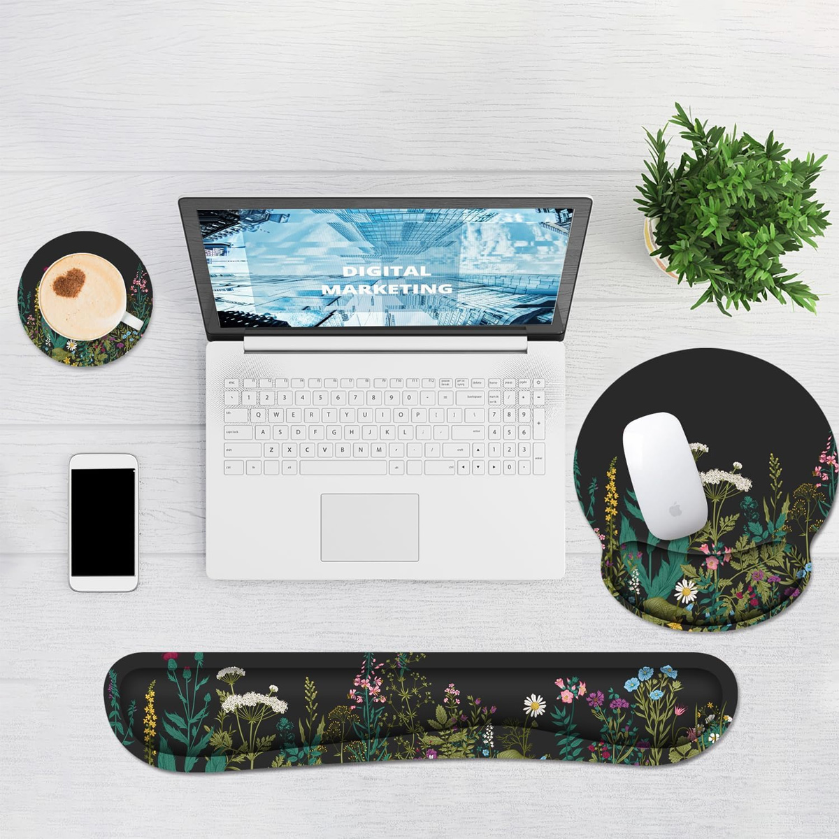 Ein Laptop mit „DIGITAL MARKETING“ auf dem Bildschirm, Maus, Handgelenkstütze, Untersetzer, Telefon und Pflanze auf weißer Holzoberfläche.
