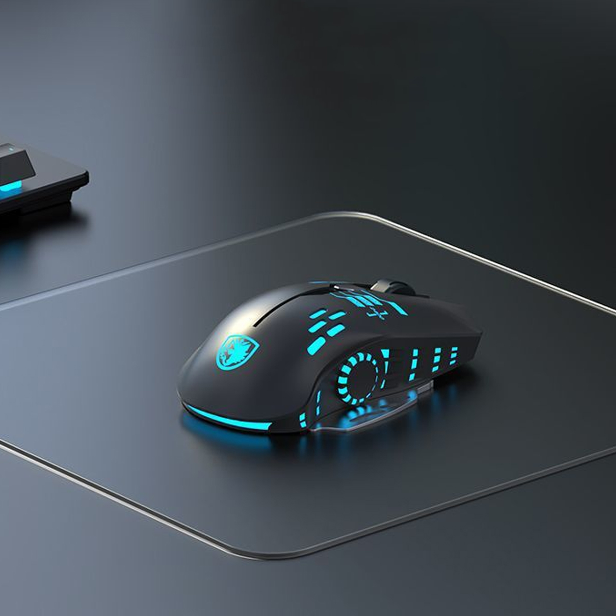 Eine schwarze Gaming-Maus mit blauen Lichtern liegt auf einem grauen Mauspad. Im Hintergrund ist eine Tastatur zu sehen. Die Szene ist gut beleuchtet.