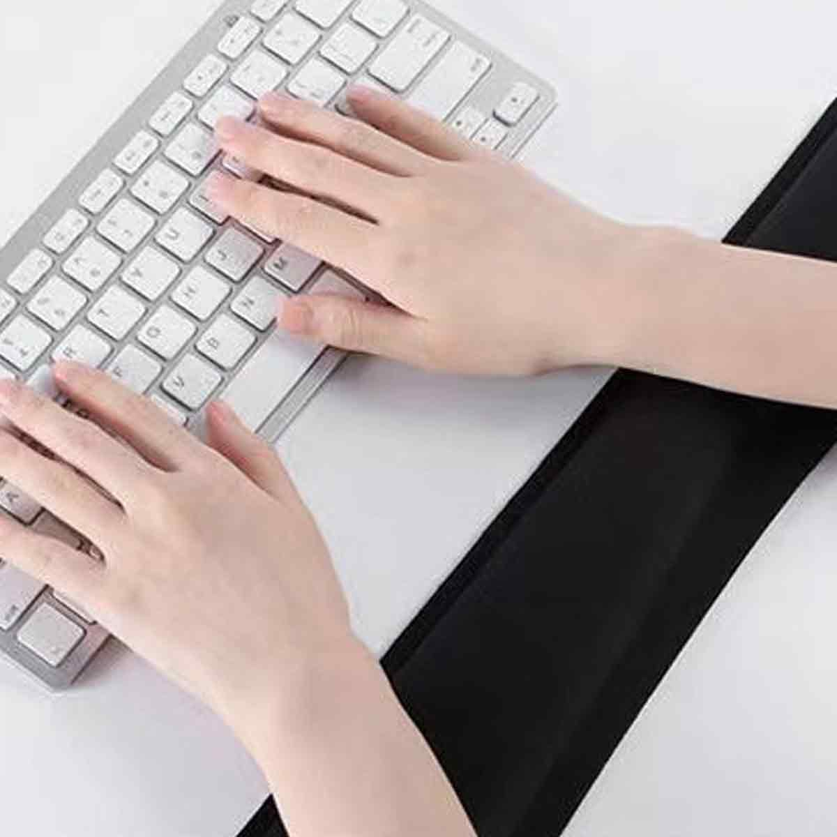 Hände tippen auf einer Tastatur mit schwarzer Handgelenkauflage. Die Tastatur liegt auf einer weißen Oberfläche. Die Hände sind hellhäutig.