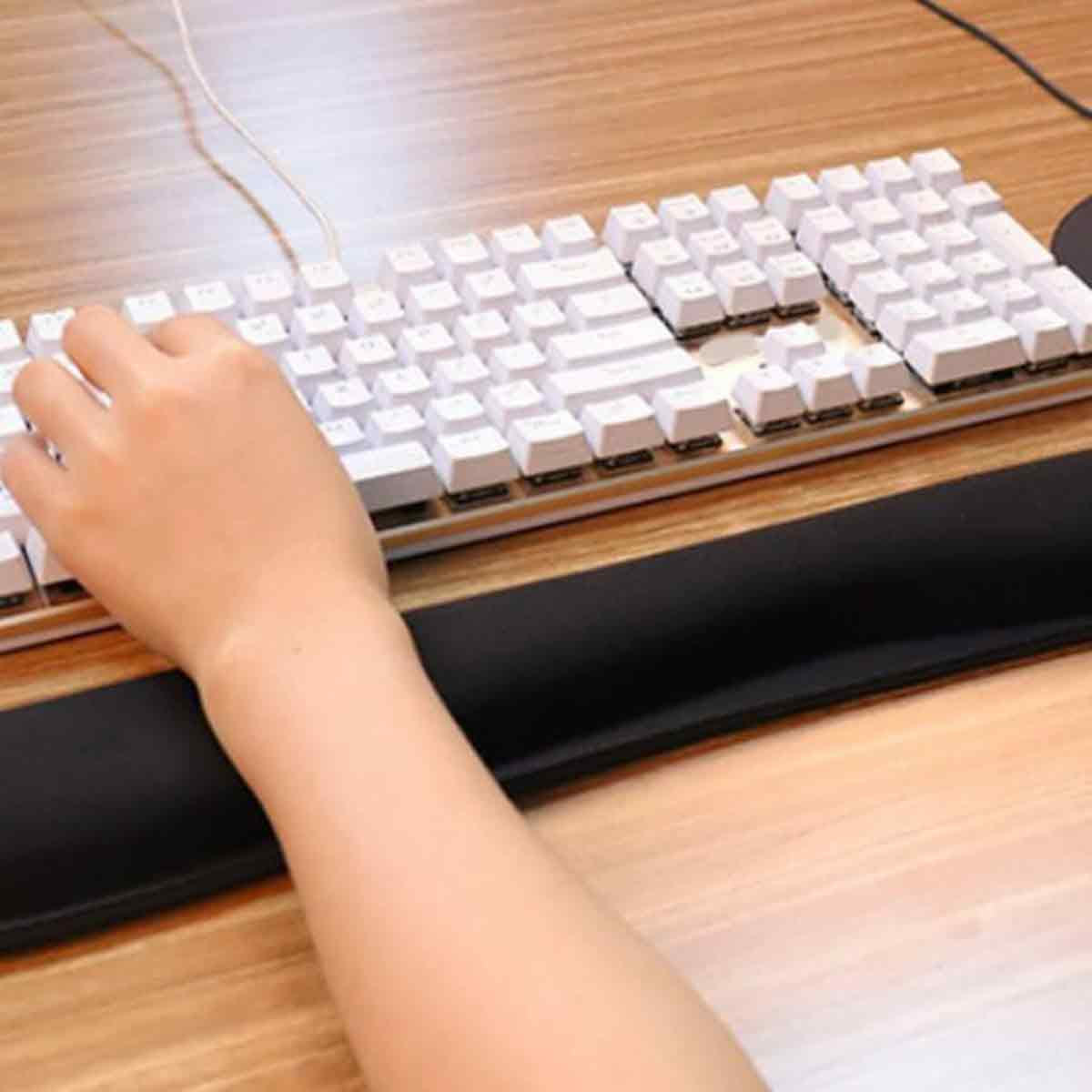 Eine Hand tippt auf einer weißen Tastatur mit einer schwarzen Handgelenkauflage auf einem Holztisch. Ein Kabel ist ebenfalls sichtbar.