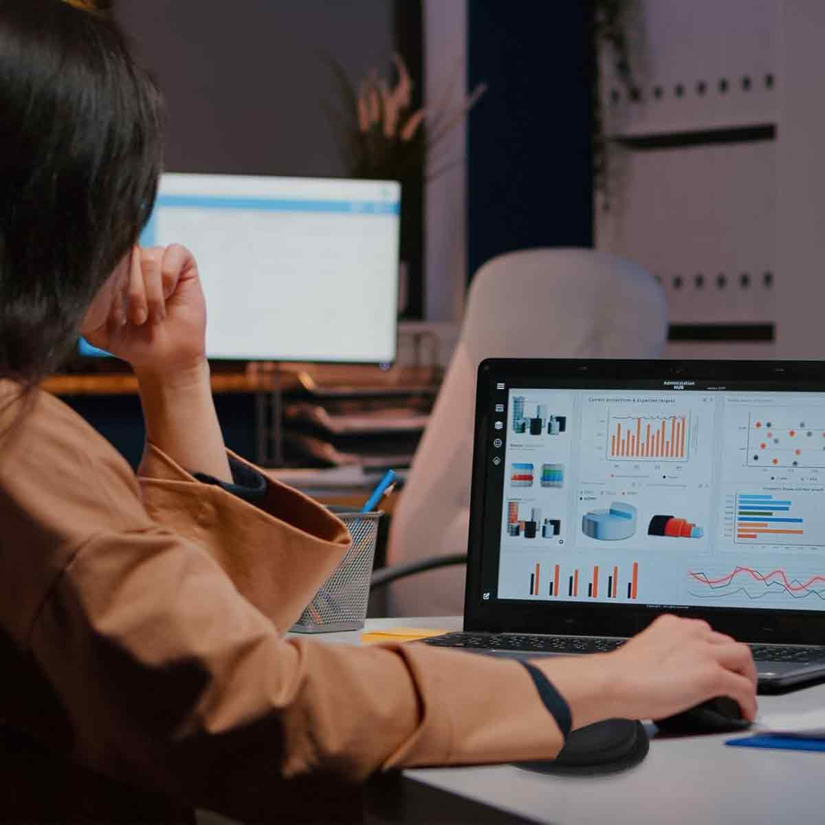 Eine Frau arbeitet an einem Schreibtisch an einem Laptop, auf dessen Bildschirm Diagramme zu sehen sind. Sie benutzt eine Maus.
