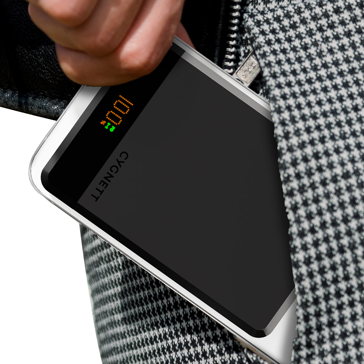 Eine Hand legt eine Powerbank in eine Tasche. Die Powerbank zeigt 100% Ladung und CYGNETT. Die Tasche hat ein Hahnentrittmuster.