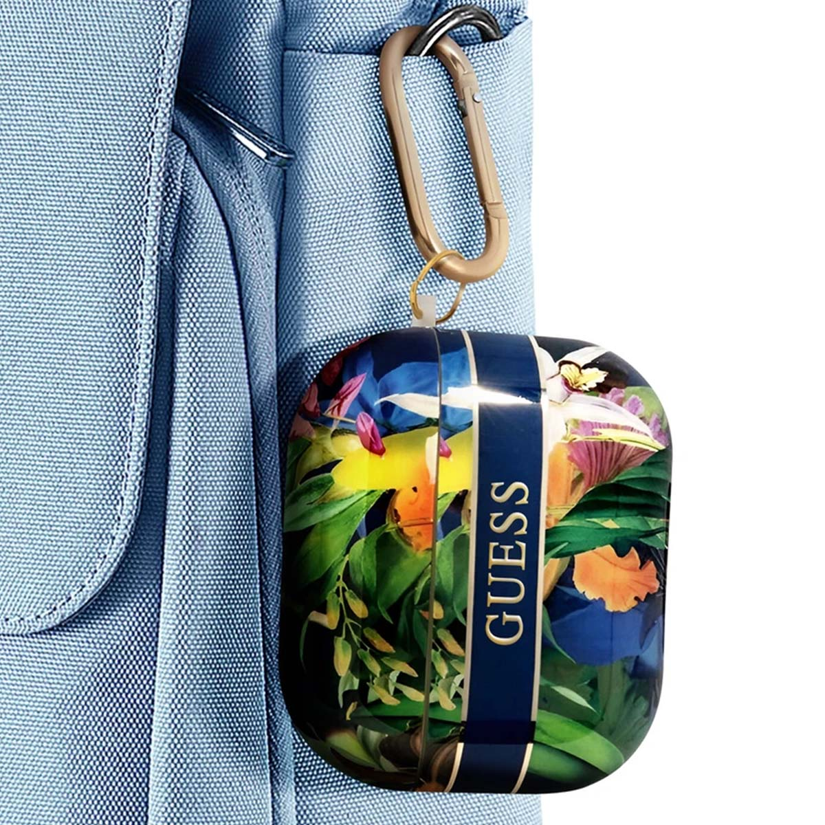 Una funda floral de AirPods GUESS cuelga de un mosquetón en una mochila azul. La funda tiene un diseño tropical con el nombre de la marca en el lateral.
