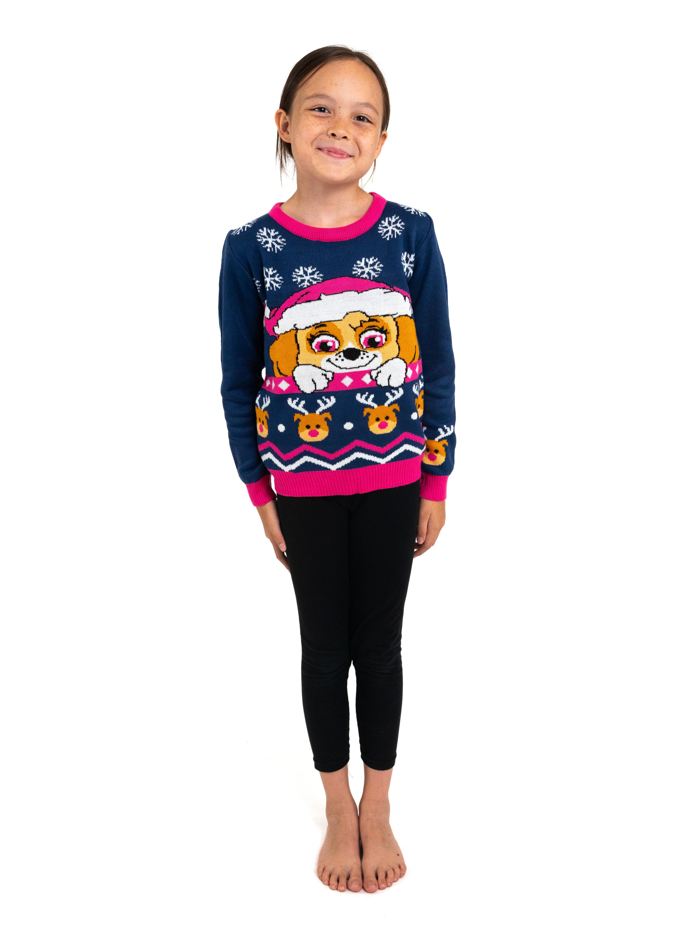 Ein Mädchen steht da, trägt einen blauen Pullover mit Hundedesign, schwarze Leggings und ist barfuß vor weißem Hintergrund.
