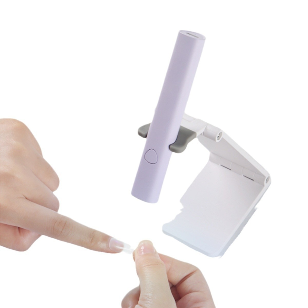 Hände halten einen Nagel-Tipp, mit einer violetten Nagellampe im Hintergrund. Die Lampe steht auf einem weißen Ständer. Weißer Hintergrund.