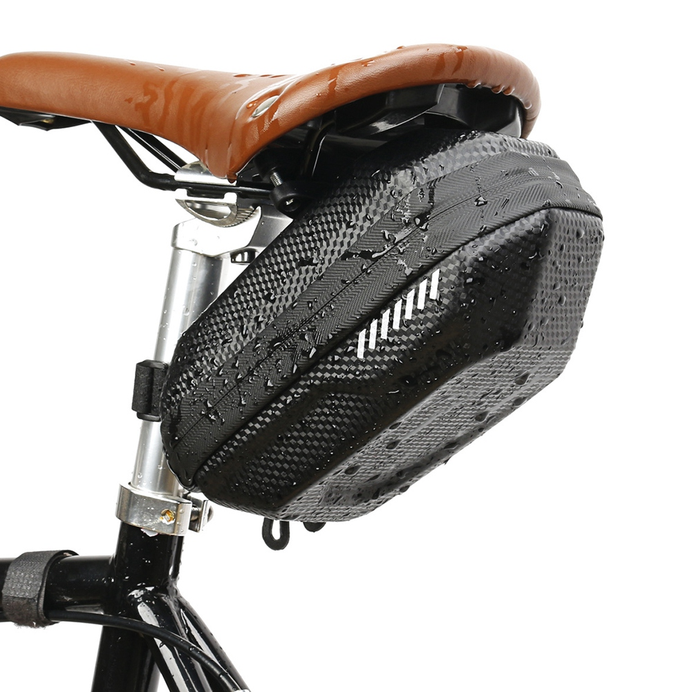 Eine schwarze Fahrrad-Satteltasche mit weißen Streifen ist unter einem braunen Ledersattel montiert. Die Tasche ist nass.