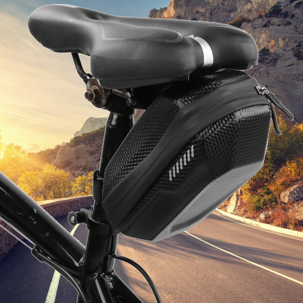 Schwarzer Fahrradsattel mit angebrachter Tasche. Straße und Berg im Hintergrund. Sonniger Tag.