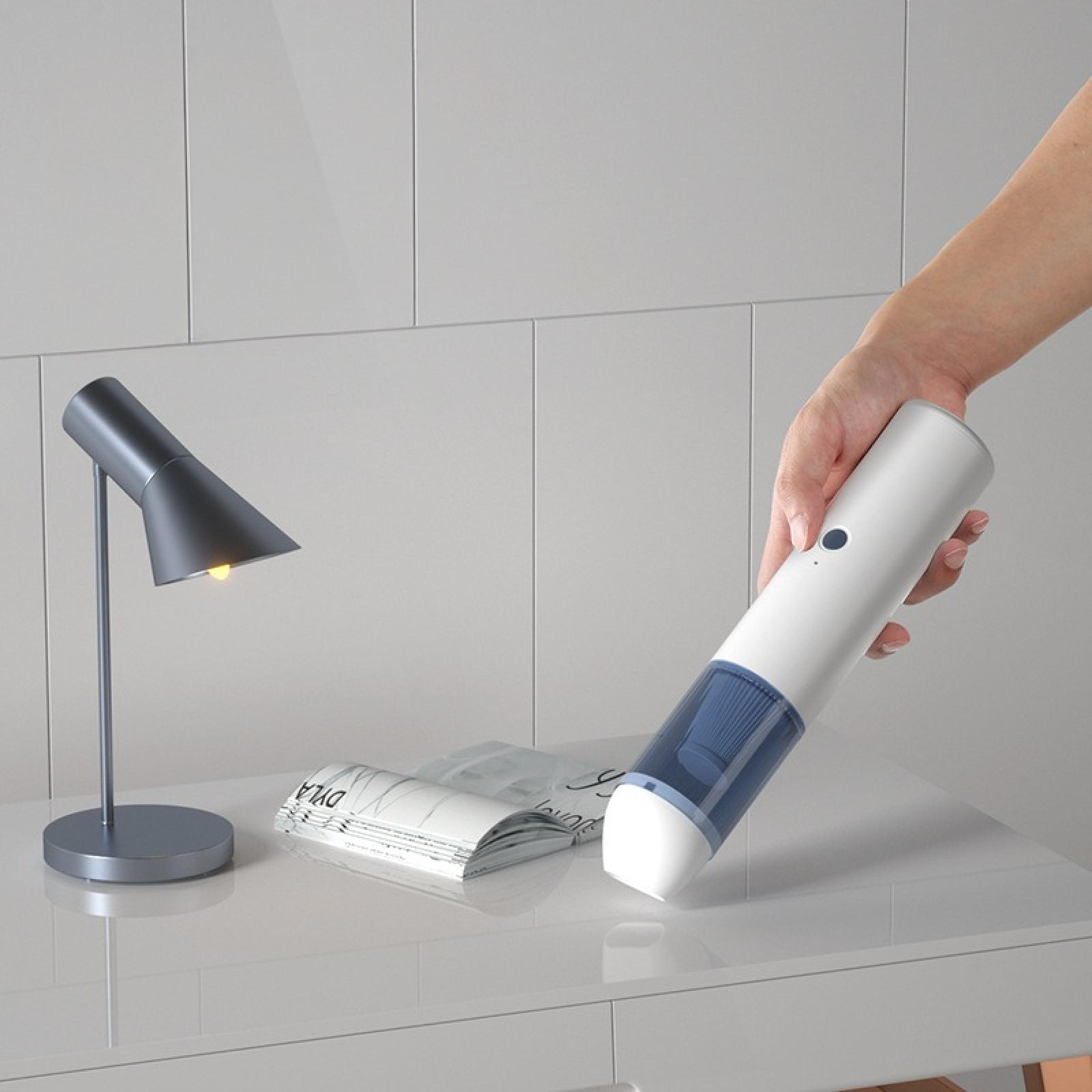 Eine Person hält einen weißen und blauen Handstaubsauger über einen weißen Tisch. Eine Lampe und eine Zeitschrift befinden sich ebenfalls auf dem Tisch.