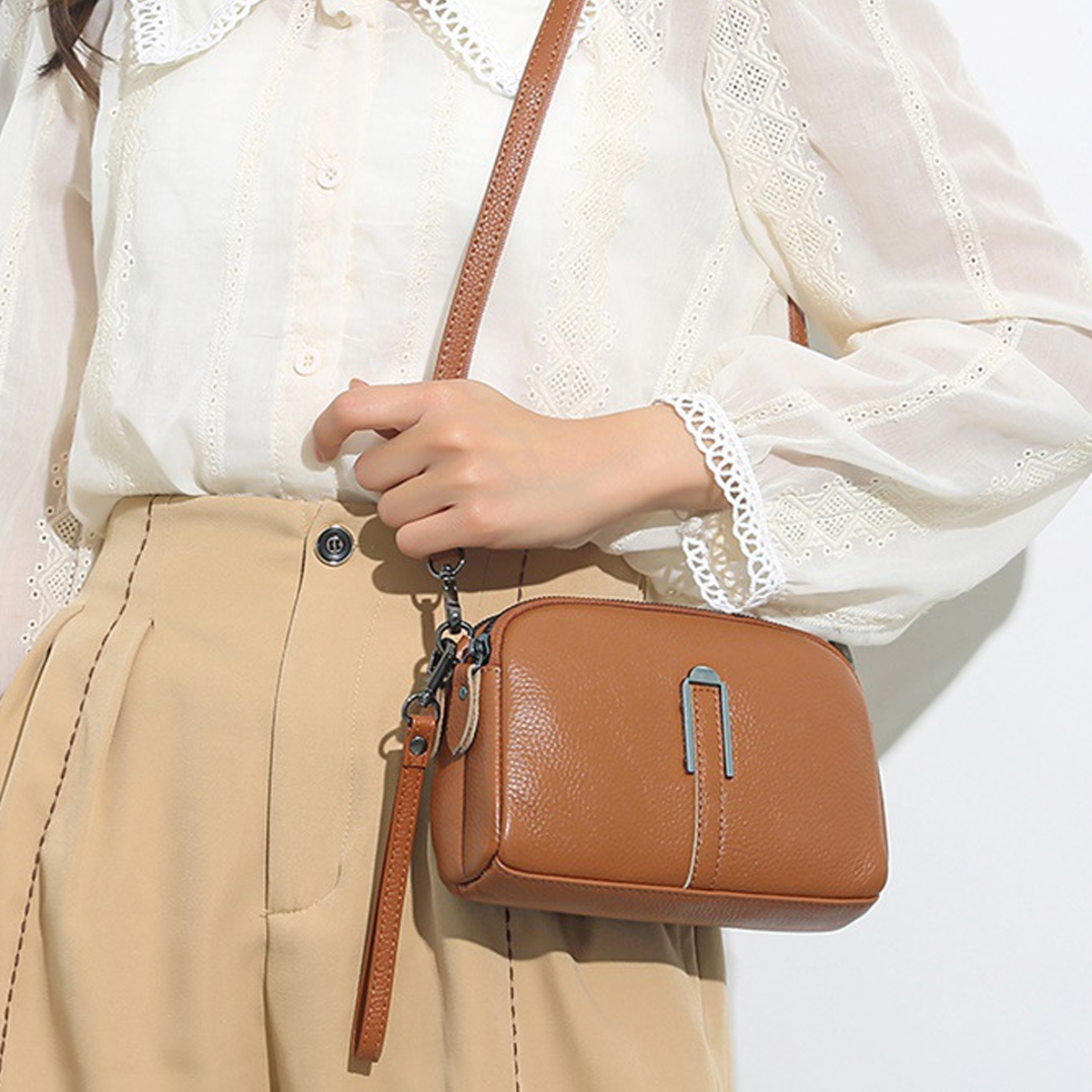 Eine Frau hält eine braune Ledertasche mit silbernem Verschluss. Sie trägt eine weiße Bluse und einen beigefarbenen Rock. Der Hintergrund ist weiß.