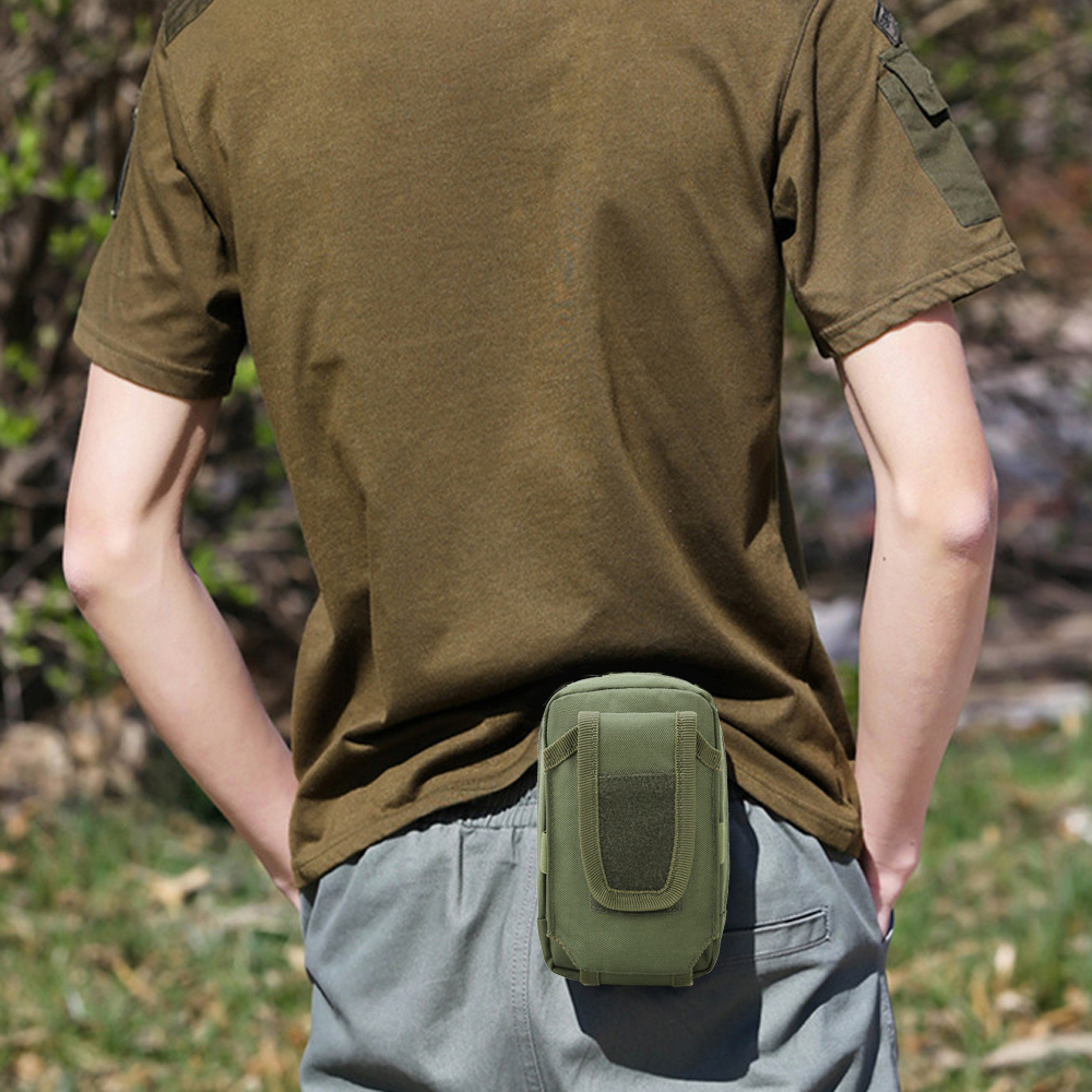 Eine Person trägt ein grünes Hemd und eine graue Hose. Ein grüner Beutel ist an der Taille der Person befestigt. Bäume sind im Hintergrund.