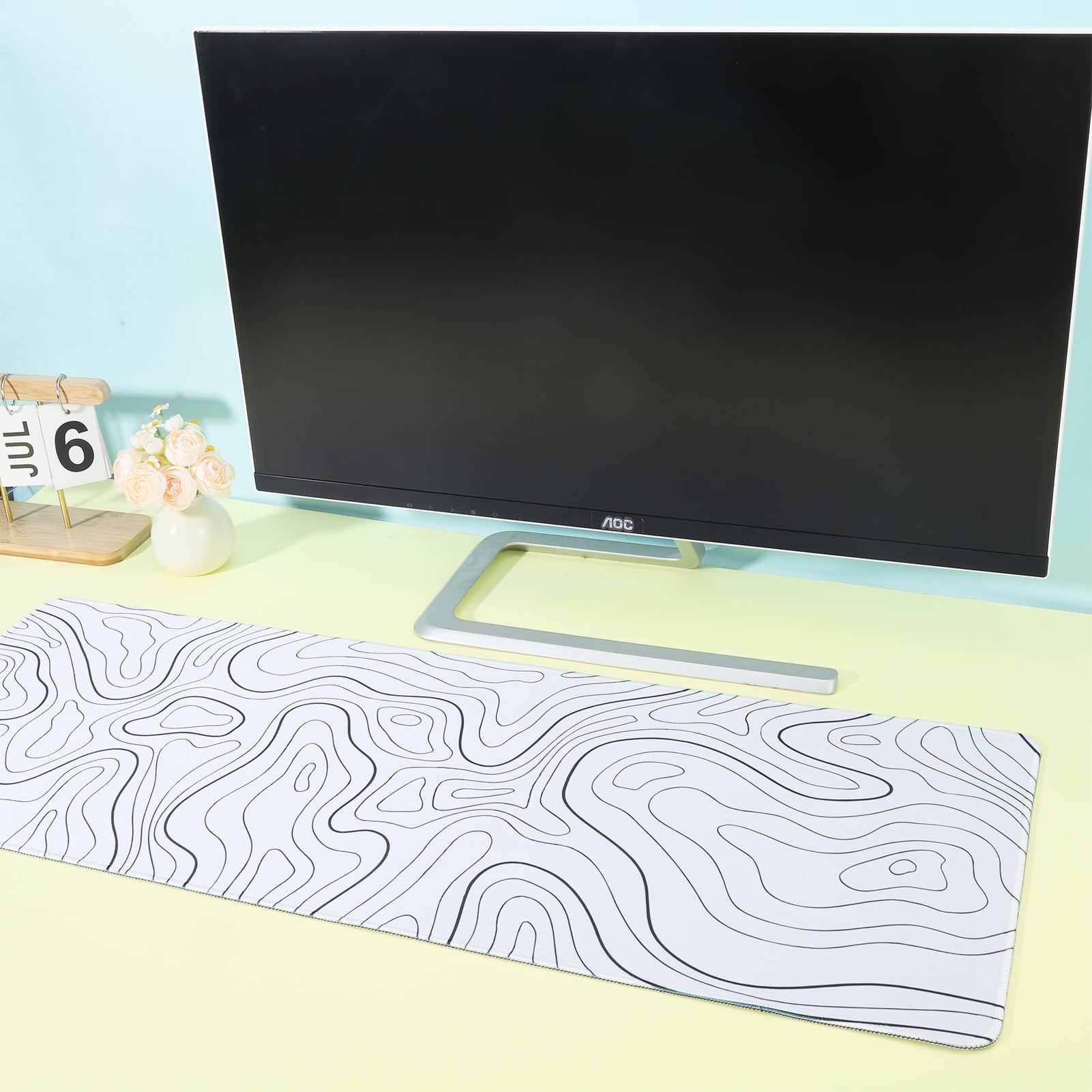 Ein Schreibtisch-Setup mit Computermonitor, Mausp Pad und Kalender. Das Mauspad hat ein topografisches Kartendesign.