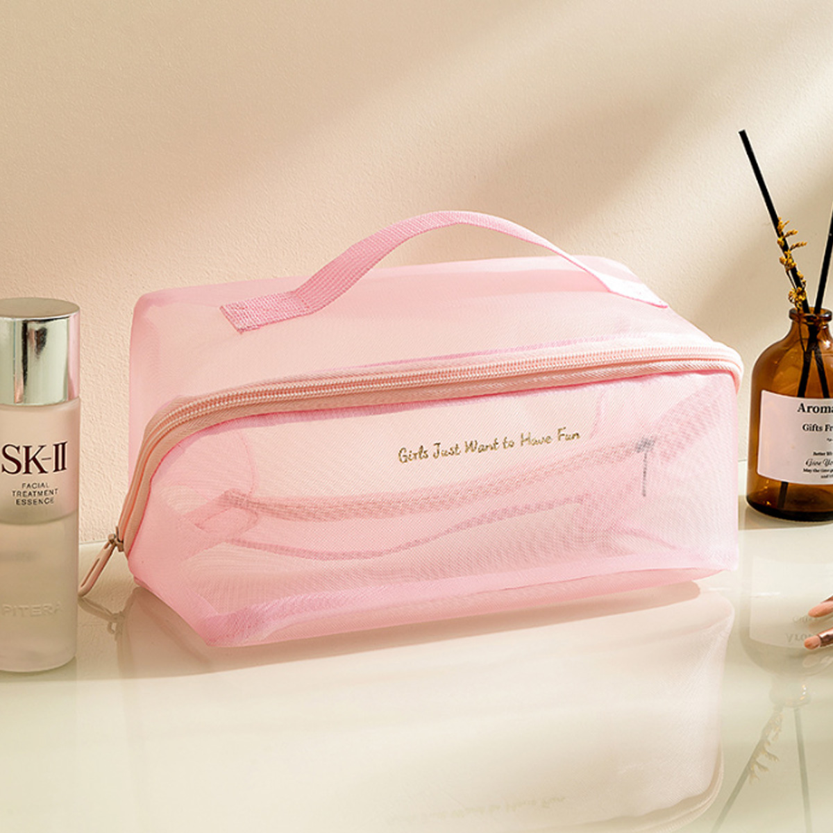 Eine rosa Kosmetiktasche mit dem Text "Girls Just Want to Have Fun", eine Flasche SK-II und ein brauner Aromadiffusor.