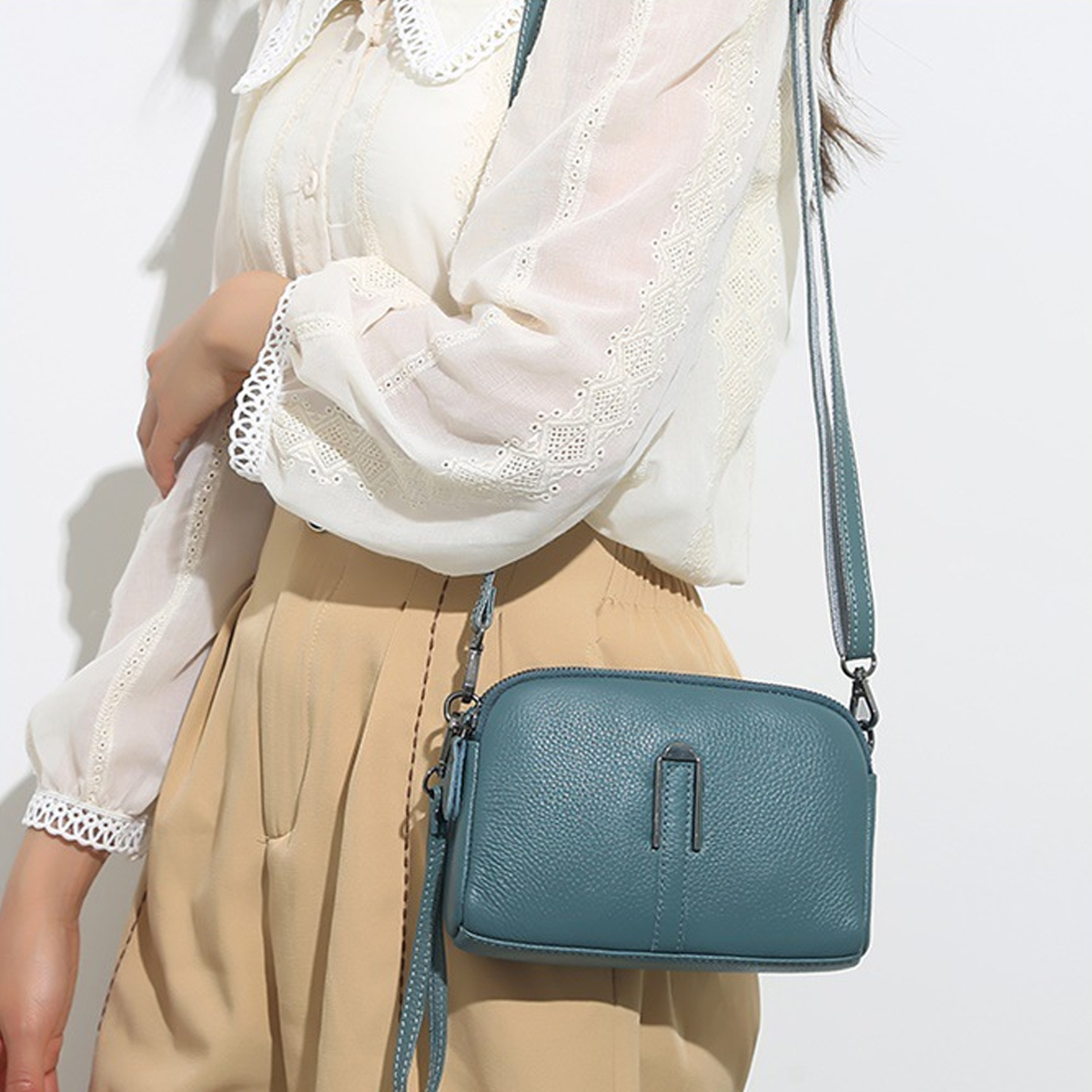 Eine Frau trägt eine weiße Bluse und einen beigen Rock und hält eine türkisfarbene Handtasche. Die Tasche hat einen langen Riemen.