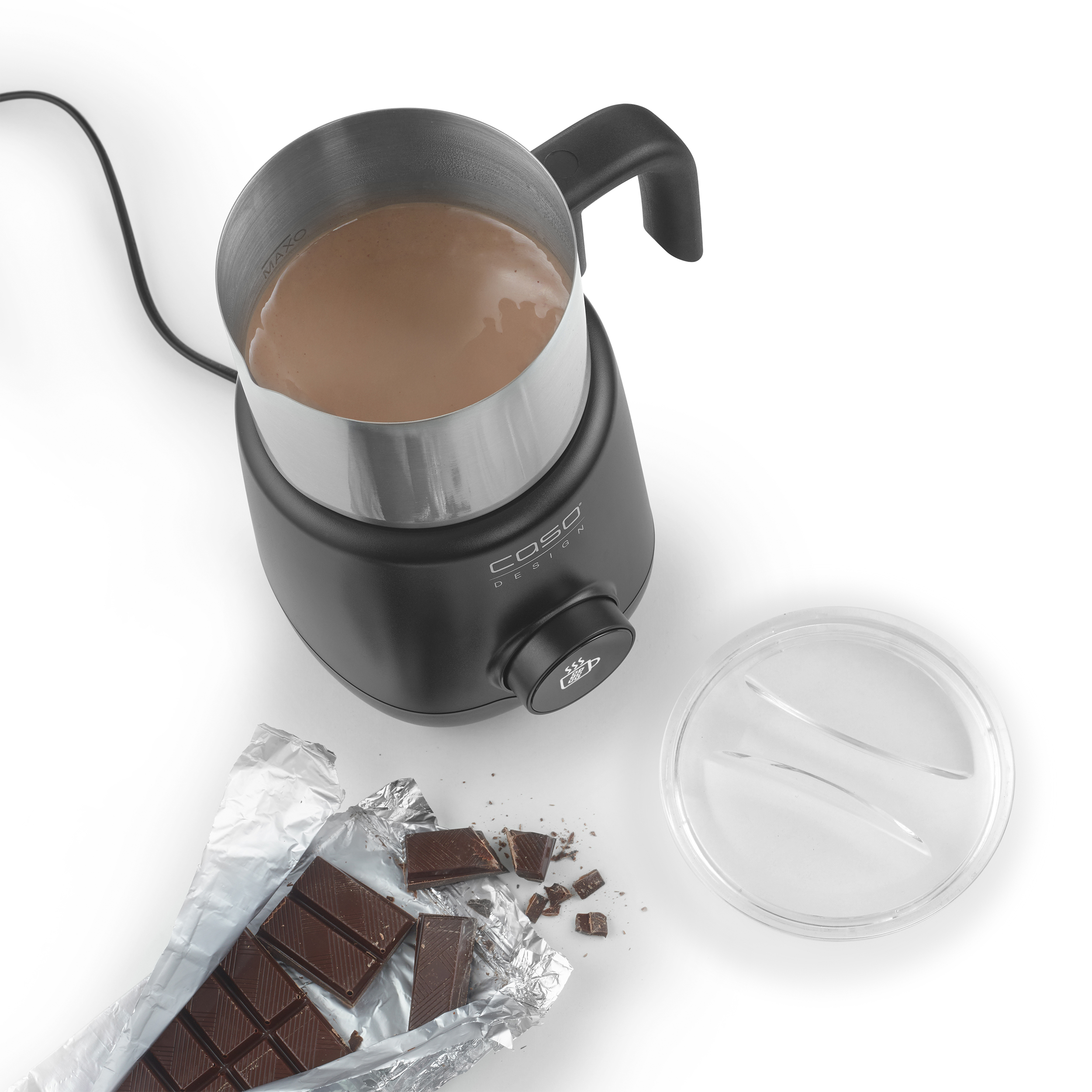 Ein schwarzer Milchaufschäumer mit Milch, eine zerbrochene Schokoladentafel und ein klarer Deckel auf weißem Untergrund.